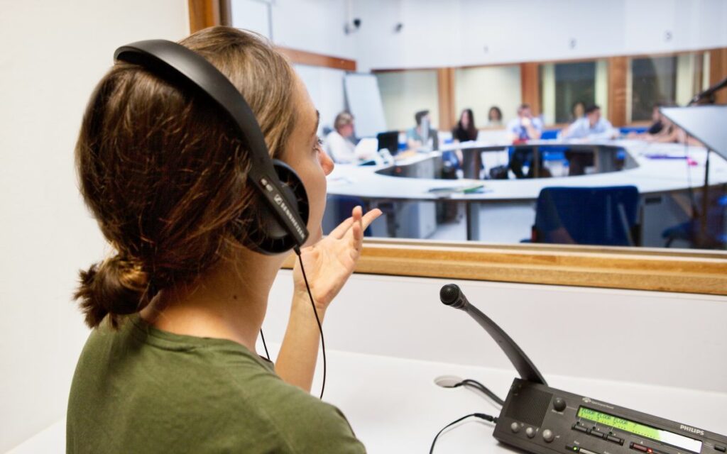Eine Studierende sitzt mit Kopfhörern in einer Dolmetschkabine: eine typische Aufgabe, wenn Sie Dolmetschen studieren.